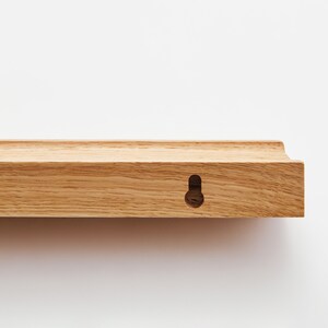 Puede incluir: Una estanter&iacute;a de madera marr&oacute;n claro con un borde redondeado y un solo agujero para colgar.