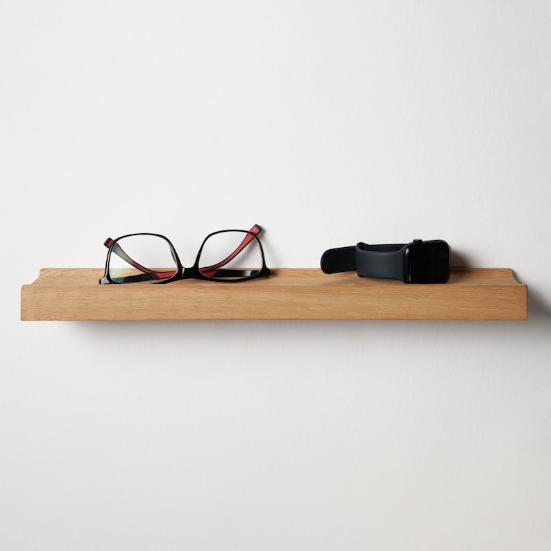 Puede incluir: Una estanter&iacute;a de madera con un par de gafas con montura negra y un reloj de pulsera negro.