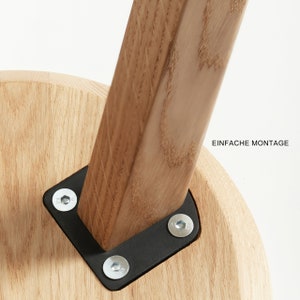 May include: Close-up of a wooden stool with a black metal bracket and screws. The bracket is attached to the underside of the stool's seat. The text "EINFACHE MONTAGE" is visible in the background.