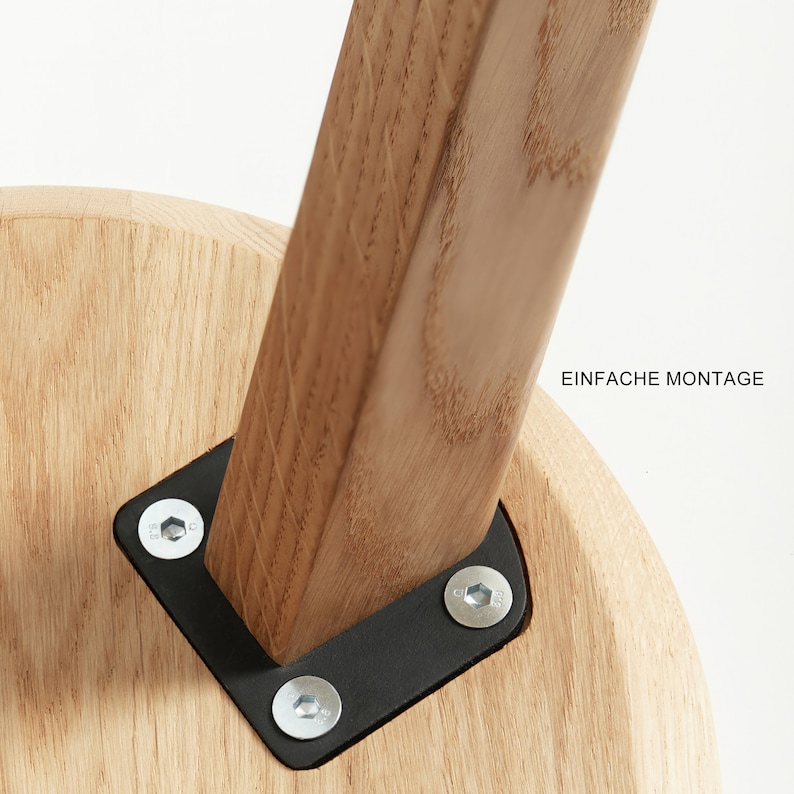 May include: Close-up of a wooden stool with a black metal bracket and screws. The bracket is attached to the underside of the stool's seat. The text "EINFACHE MONTAGE" is visible in the background.