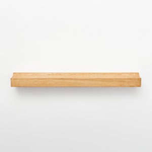 Puede incluir: Una estanter&iacute;a de madera natural con bordes redondeados. La estanter&iacute;a est&aacute; montada en una pared blanca.