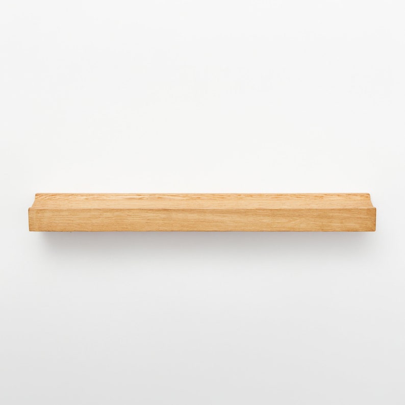 Puede incluir: Una estanter&iacute;a de madera natural con bordes redondeados. La estanter&iacute;a est&aacute; montada en una pared blanca.