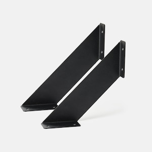 Puede incluir: Dos soportes de estante de metal negro, cada uno con una forma triangular y una base plana. Los soportes están inclinados hacia arriba y están diseñados para soportar un estante.