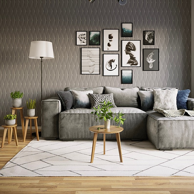 May include: A gray sectional sofa with a white and gray patterned rug, a wooden coffee table, and a floor lamp. The wall behind the sofa is decorated with a gallery wall of black framed artwork.
