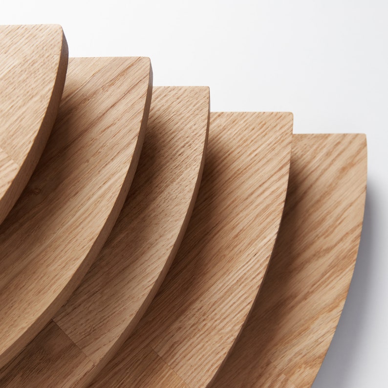 May include: A set of five wooden serving trays, each with a rounded edge and a natural wood grain finish. The trays are stacked in a graduated size, creating a visually appealing display.