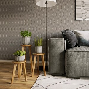 May include: Three wooden plant stands with three potted plants. The stands are stacked on top of each other, with the largest stand at the bottom and the smallest stand at the top. The plants are all green and leafy. The stands are in front of a gray wall with a diamond pattern. A gray couch is in the background.