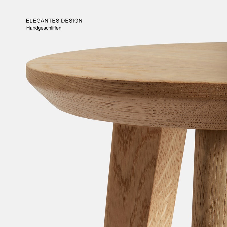 May include: A close-up of a light wood round table with three legs. The table top has a slightly rounded edge. The text "ELEGANTES DESIGN" and "Handgeschliffen" is visible in the top left corner of the image.
