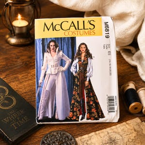Puede incluir: Patrón de costura McCall's Costumes M6819, con ilustraciones de dos diseños de disfraces. El patrón incluye tallas E5 (14-16-18-20-22). La portada muestra a una mujer con un atuendo blanco y otra con un vestido floral.