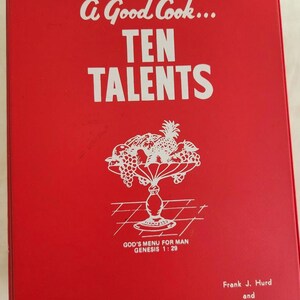 May include: A red cookbook with the title "A Good Cook... TEN TALENTS" in white lettering, featuring a white illustration of a fruit bowl. The text "GOD'S MENU FOR MAN GENESIS 1:29" is also visible. Authors' names are at the bottom.