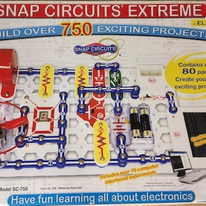 May include: Snap Circuits Extreme electronics kit box featuring over 750 projects and 80 parts. The packaging displays a white circuit board with blue, red, and yellow components, a red fan, a solar cell, and a digital display. Model SC-750.