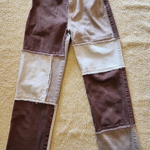 May include: Patchwork jeans in shades of brown, tan, and cream. The denim pants feature a high waist and a straight leg design. The patchwork design is visible on the front and back of the jeans.