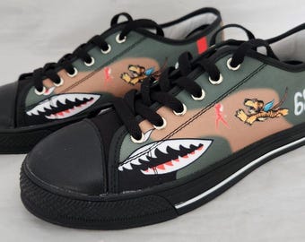 May include: A pair of black canvas trainers with a camouflage print featuring a shark tooth design and a cartoon tiger. The trainers have a white stripe around the sole and the number "68" on the side.