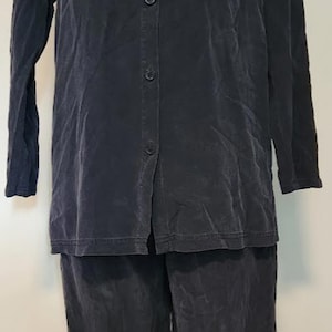 Könnte beinhalten: Ein zweiteiliges Outfit in Dunkelmarineblau. Das Oberteil ist ein langärmliges Button-Down-Hemd mit zwei Brusttaschen. Die passende Hose ist weit geschnitten. Der Stoff hat eine leicht zerknitterte Textur.