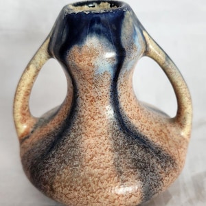 Peut inclure: Un petit vase en céramique avec deux anses. Le vase est décoré d'un glaçage marbré dans les tons de brun, bleu et blanc.