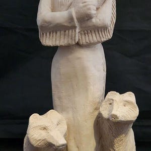 May include: A white ceramic sculpture of a Native American woman holding a small bird in her arms. Two white ceramic wolves stand on either side of her.