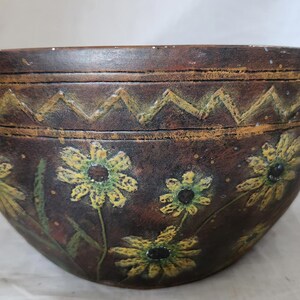 Puede incluir: Un cuenco de cerámica marrón con un diseño decorativo de flores amarillas y hojas verdes. El cuenco tiene dos pequeñas asas a los lados.