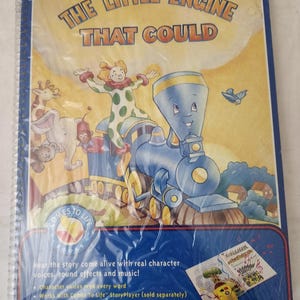 Könnte beinhalten: Kinderbuch mit dem Titel "The Little Engine That Could" mit einer Illustration einer blauen Lokomotive. Das Cover zeigt einen Clown, verschiedene Tiere und den Text "COMES TO LIFE". Enthält einen kleinen Einsatz mit einem gelben Gerät und Noten. Ab 3 Jahren.