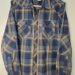 May include: A blue, yellow, and gray plaid button-down shirt with two chest pockets and elbow patches. The shirt has long sleeves and a collar. The brand label "L.L.Bean" is visible at the top.