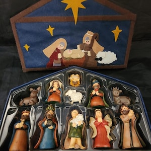 May include: A Christmas nativity set featuring a blue felt stable with a gold star and figures of Mary, Joseph, and baby Jesus. The set includes figurines of the three wise men, an angel, and other characters.