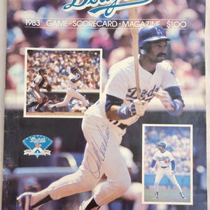 May include: A 1983 Los Angeles Dodgers game scorecard and magazine. The cover features a photo of a baseball player in a Dodgers uniform, holding a bat and wearing a cap with the team's logo. The player's signature is visible in the lower left corner. The text "Dodgers" is printed in blue at the top of the cover, and the text "1983 GAME SCORE CARD MAGAZINE $1.00" is printed below it.