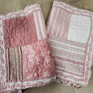 May include: Two rectangular quilted fabric pieces featuring a patchwork design in shades of red, white, and beige. The patterns include floral motifs, vertical stripes, and solid blocks, all finished with a decorative scalloped border edge.