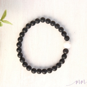 May include: Black beaded bracelet with a white bead and a black lava bead.