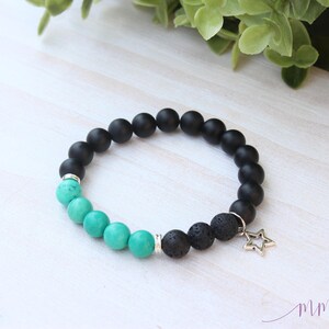 May include: A black and turquoise beaded bracelet with a silver star charm. The bracelet is made with black lava rock and turquoise beads.