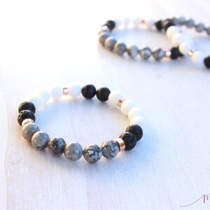 May include: Three bracelets made with grey, white and black beads. The bracelets are made with lava rock, white howlite and grey jasper beads. The bracelets are separated by a small space on a white wooden surface.