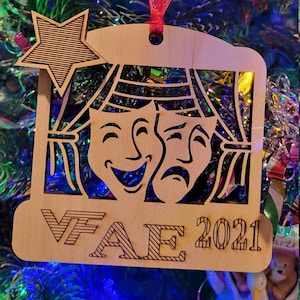 May include: A wooden Christmas bauble featuring a star, two masks, and the text "VFAE 2021".
