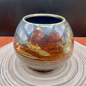 May include: A white ceramic mug with a black handle and the text "But First, Coffee" in a handwritten style. The mug is on a white surface. The mug is 4 inches tall.