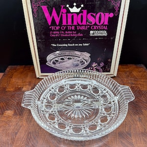 May include: A clear glass divided relish dish with a central divider, featuring a starburst pattern at the base and a geometric rim design. The original packaging box is visible behind the dish, labeled Windsor Top O' The Table Crystal.