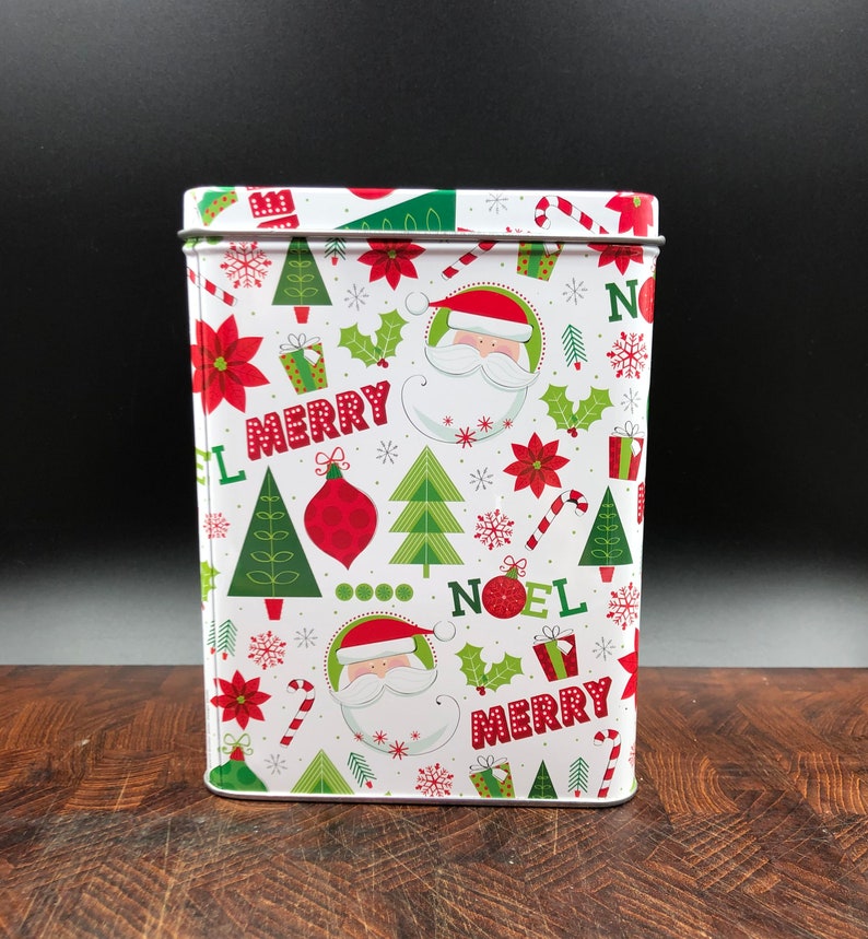 May include: Rectangular metal tin with a festive Christmas pattern. The design includes Santa Claus faces, Christmas trees, poinsettias, holly, and the words "MERRY" and "NOEL" in red and green on a white background.