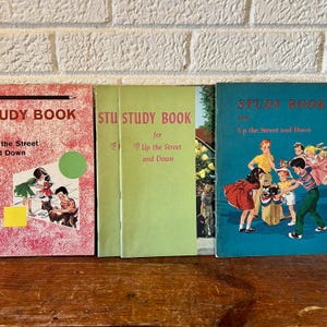 May include: Three vintage children's study books with colorful covers. The book on the left has a red cover with a picture of children playing on the street. The middle book has a green cover with the text "STU STUDY BOOK for Up the Street and Down". The book on the right has a blue cover with a picture of children playing on the street and the text "STUDY BOOK Up the Street and Down".