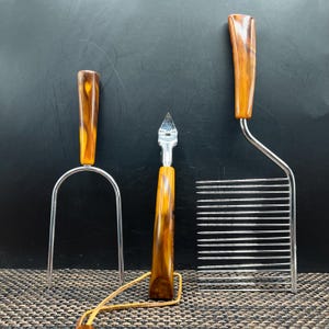 May include: A set of three vintage kitchen tools with brown and yellow marbled handles. Includes a cake cutter, a fork, and a bottle opener. The metal parts are silver-toned.