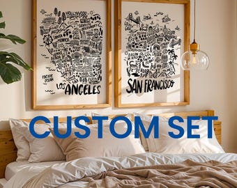 May include: Two framed art prints with detailed black and white illustrations of Los Angeles and San Francisco landmarks. The prints are in light wood frames and hang above a bed with neutral-colored bedding. The text "CUSTOM SET" is displayed in blue.