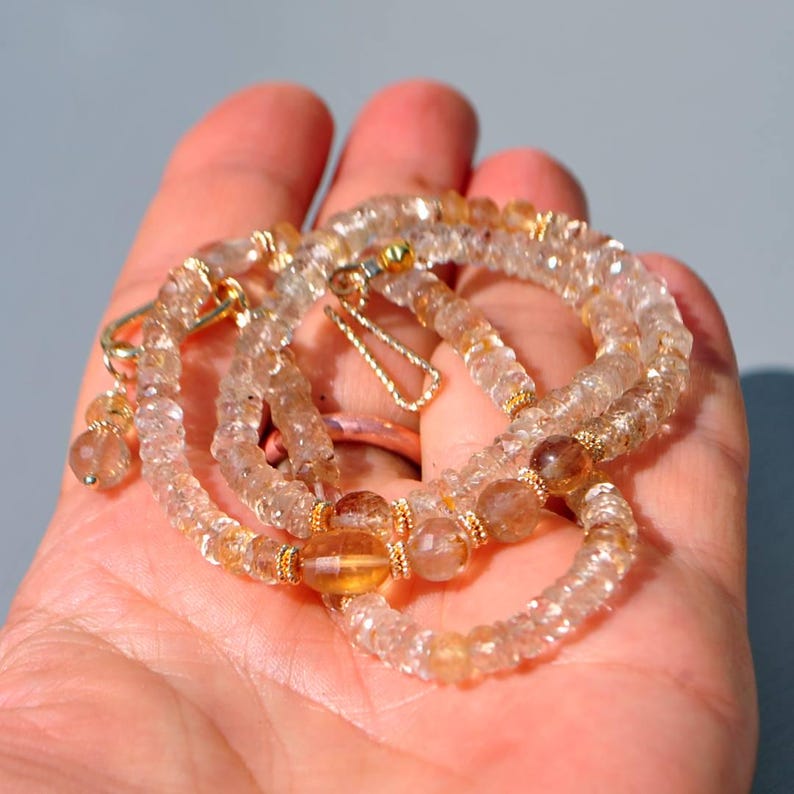 May include: A necklace composed of faceted, translucent light amber and clear beads. The strand features small gold-toned metal spacers between select beads and includes a gold-toned metal hook clasp with a dangling bead accent.