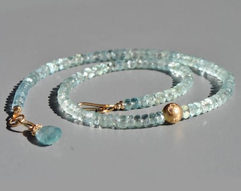 May include: A delicate aquamarine necklace with a gold clasp and a teardrop-shaped pendant. The necklace features small, faceted aquamarine beads and a gold sphere accent. The design is elegant and suitable for various occasions.