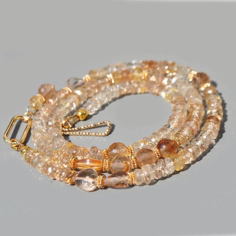 May include: A necklace composed of faceted, translucent light amber and golden-brown beads. The strand features small, round, textured gold-tone spacers and a gold-tone metal clasp with a rectangular link and a hook closure mechanism.