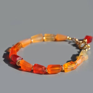 Può includere: Un braccialetto con una serie di perline rettangolari arancioni e gialle. Le perline sono collegate con una chiusura color oro e piccole perline color oro. Il colore delle perline varia dal rosso-arancio al giallo pallido.