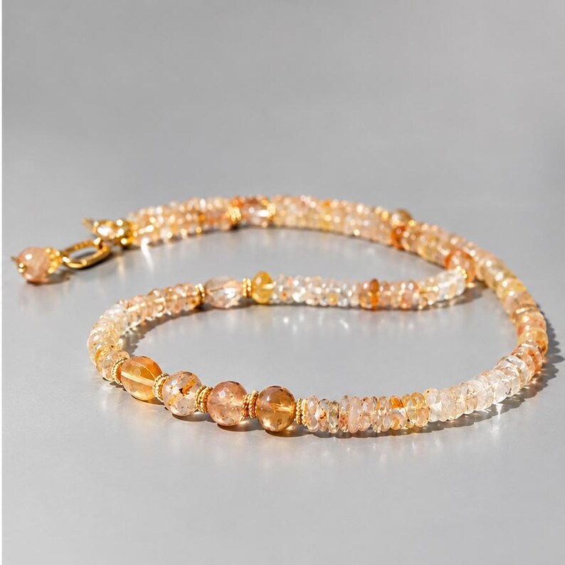 May include: A beaded necklace featuring translucent, faceted golden and amber-toned gemstones. The strand is interspersed with small, textured gold-colored metal spacers and finished with a gold-colored metal clasp at the end of the chain.