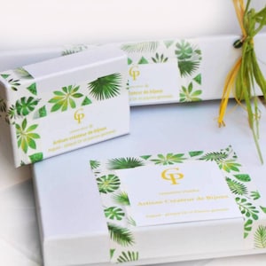 May include: Two white rectangular gift boxes decorated with green tropical leaf patterns. Each box features a central white label with a gold CP logo and the text Artisan cr&eacute;ateur de bijoux, Argent, plaqu&eacute; Or et pierres gemmes.