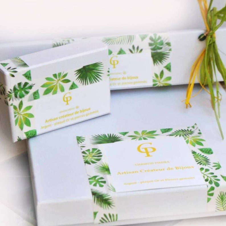 May include: Two white rectangular gift boxes decorated with green tropical leaf patterns. Each box features a central white label with a gold CP logo and the text Artisan cr&eacute;ateur de bijoux, Argent, plaqu&eacute; Or et pierres gemmes.