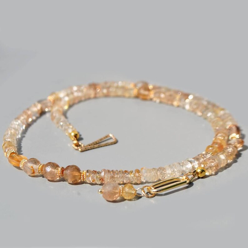 May include: A necklace composed of faceted, translucent amber and honey-colored gemstone beads. The strand features small, round beads interspersed with gold-toned metal spacers and a gold-toned oval clasp closure at the end.