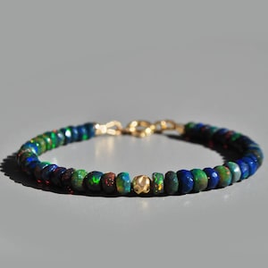 Peut inclure: Un bracelet de perles avec un mélange de perles d'opale colorées dans des tons de bleu, vert et rouge. Le bracelet a un fermoir doré et une perle dorée au centre. Les perles d'opale mesurent environ 0,5 cm de diamètre.