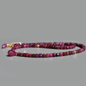 Peut inclure: Un collier composé de petites perles de rubis carrées de différentes nuances de rouge et de violet. Le collier a un fermoir doré et un pendentif en rubis en forme de goutte. Les perles sont enfilées pour créer un bijou délicat et élégant.