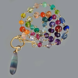 Peut inclure: Un collier coloré avec un motif en spirale de perles de pierres précieuses multicolores. Il comporte un fermoir doré et un pendentif en forme de goutte avec des nuances de bleu et de vert. Les pierres précieuses comprennent des teintes de rouge, orange, jaune, vert, bleu et violet.