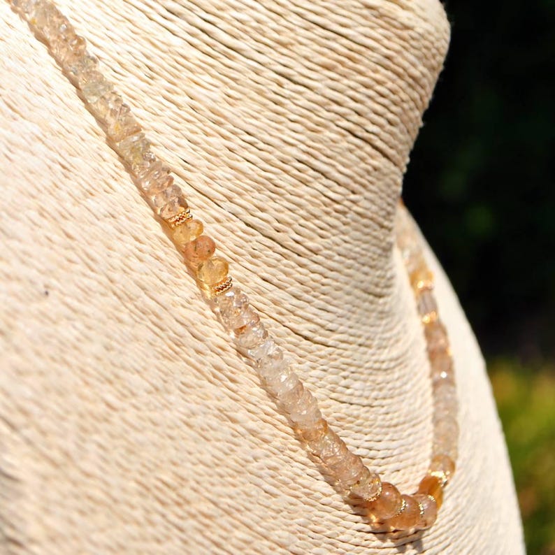 May include: A necklace composed of small, faceted, translucent light amber and clear gemstone beads. The strand features intermittent gold-toned metal spacer rings between the beads, creating a subtle, repeating pattern along the length of the jewelry.