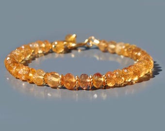 May include: A bracelet composed of faceted, translucent orange-yellow gemstone beads. The circular strand features small, metallic gold-toned spacer beads between the stones and includes a gold-toned metal lobster claw clasp closure.