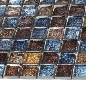 Könnte beinhalten: Eine Fliese aus irisierendem Glasmosaik in den Farben Blau, Braun und Gold. Die Fliesen sind klein und quadratisch und haben eine strukturierte Oberfläche.