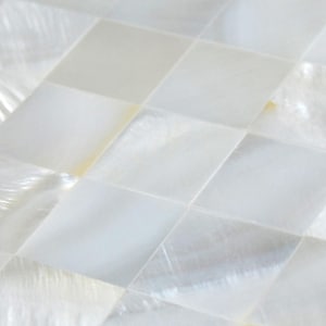 May include: White mother of pearl tile mosaic with a square pattern. The tiles are arranged in a staggered pattern, creating a diamond-like effect.